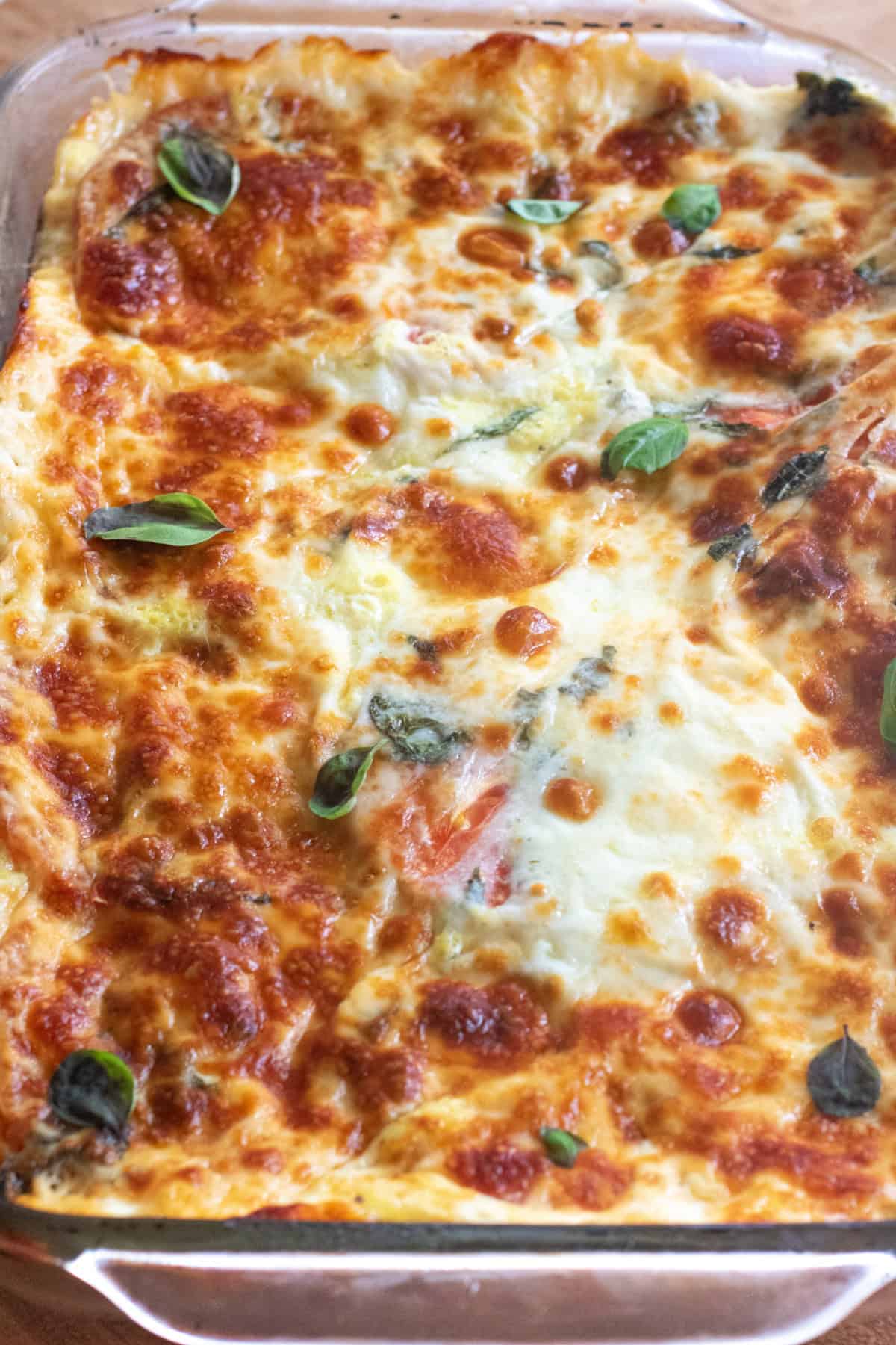 an overhead of a cheesy baked casserole with fresh basil.