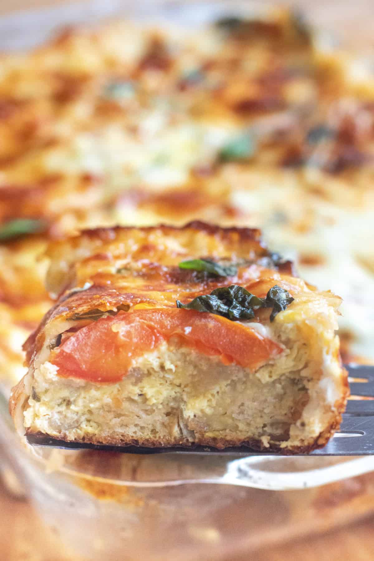 a slice of egg baguette with tomatoes and cheese and basil taken out of a tray.