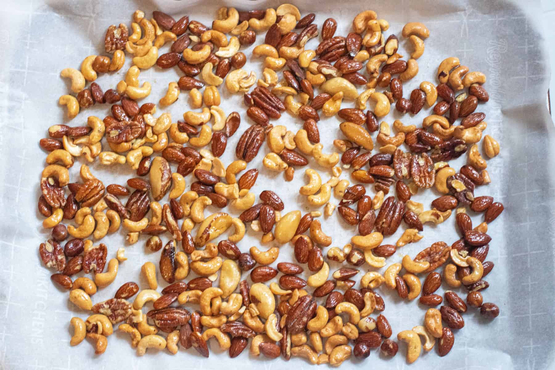 a tray of mixed nuts coated in oil on parchment paper.