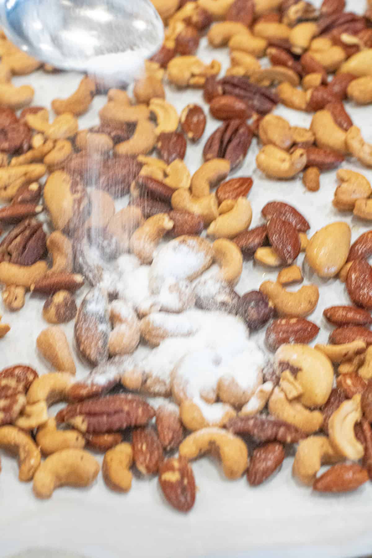 vinegar powder being sprinkled on a tray of nuts.