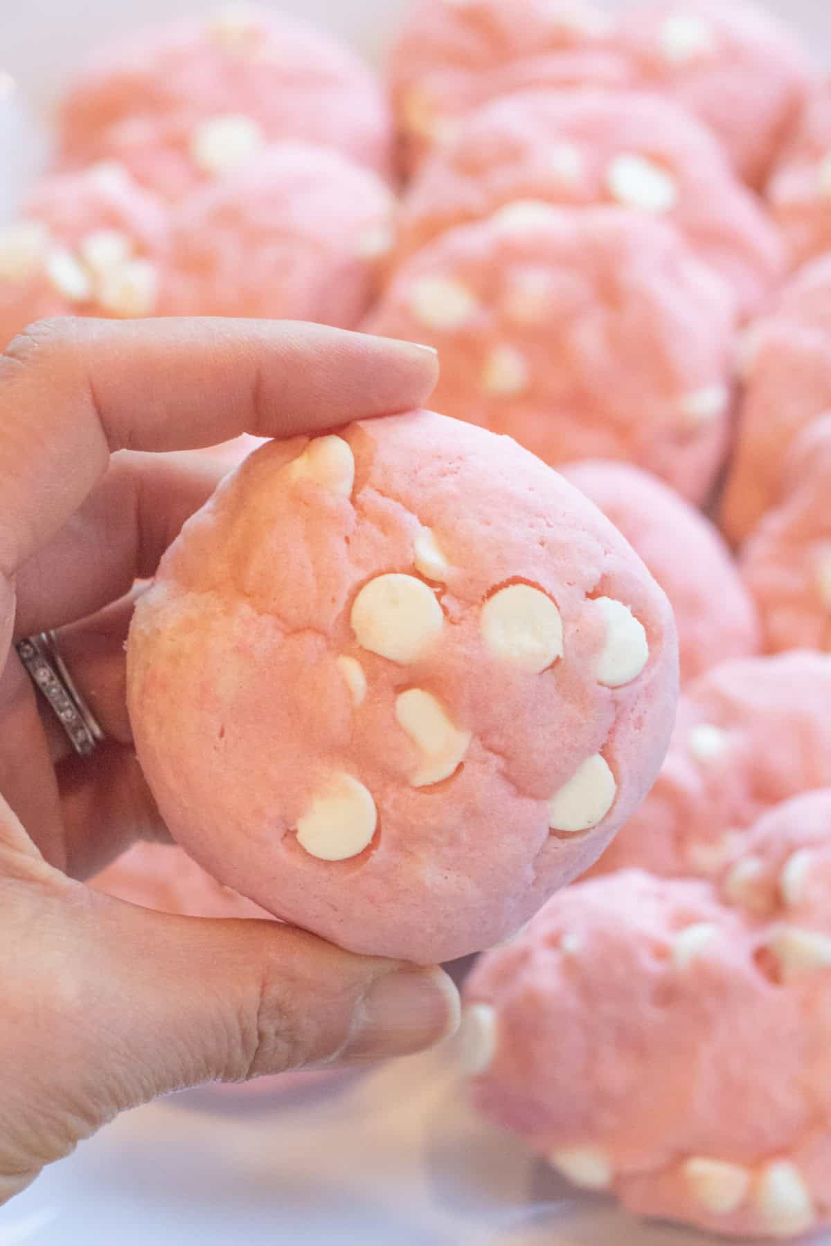 a hand holding a circular pink cookie with white chocolate chips.
