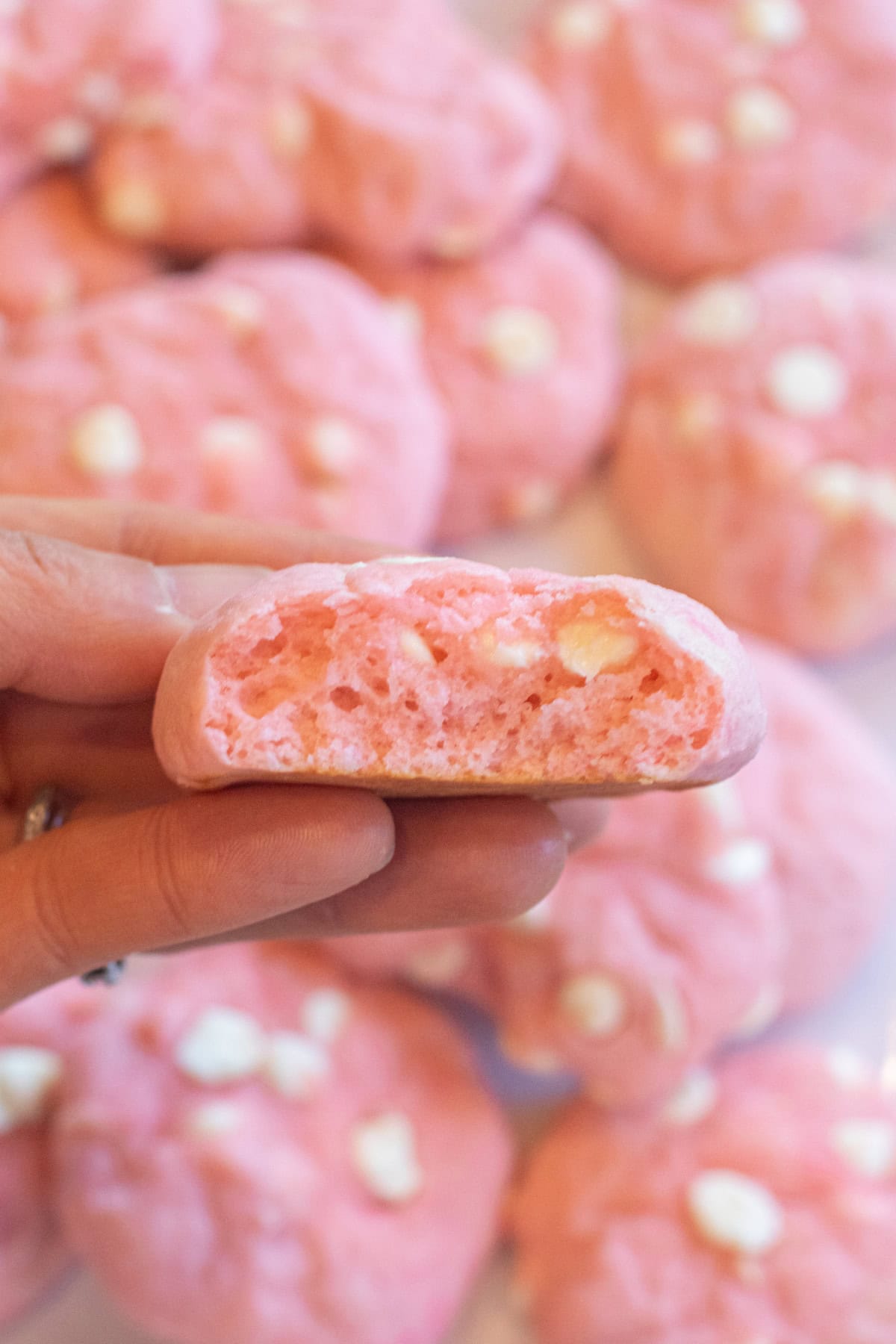 a hand holding a pink cookie with white chocolate chips and a bite taken out.