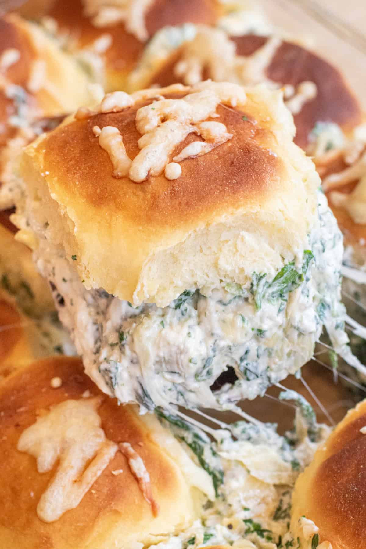 a cheese spinach artichoke dip slider being taken out of a tray of sliders.
