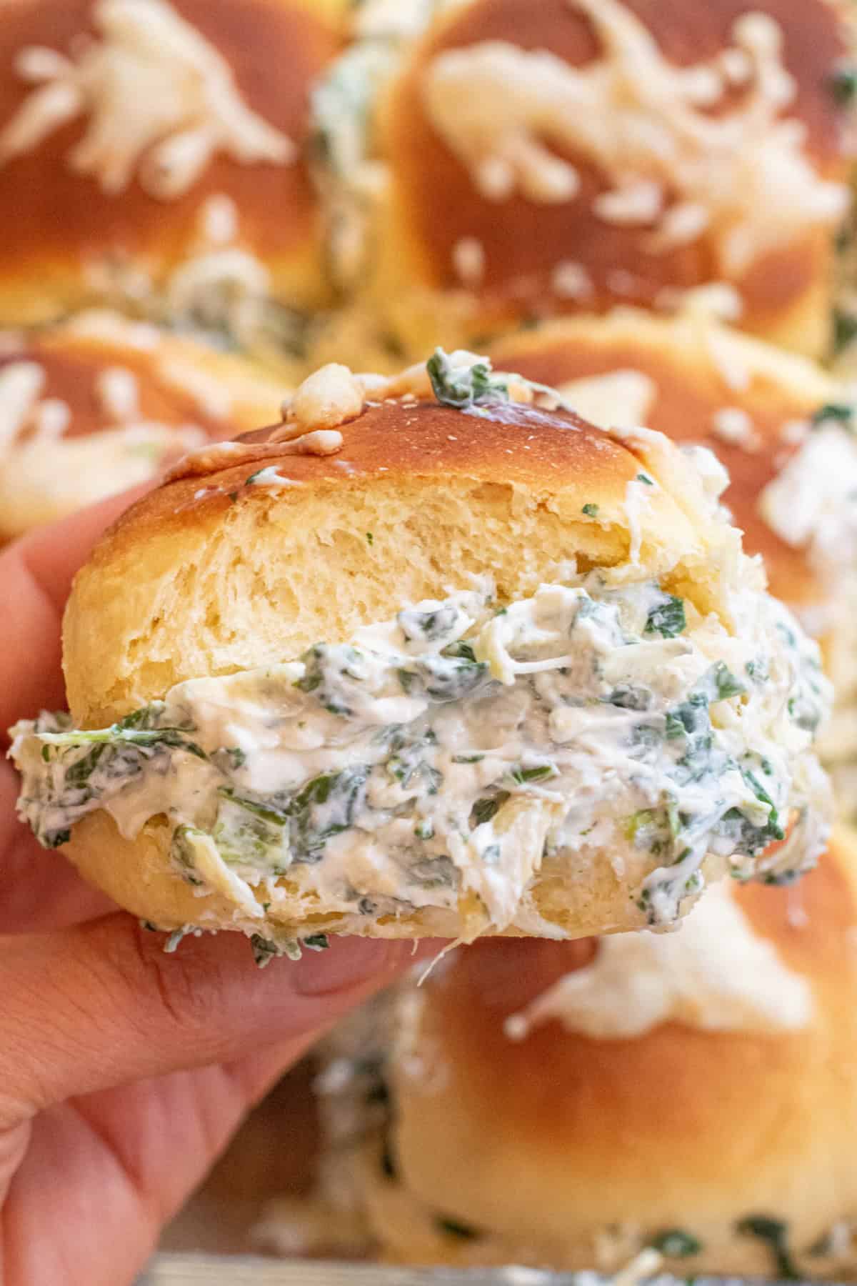 a hand holding a slider with spinach and artichoke dip on the inside.