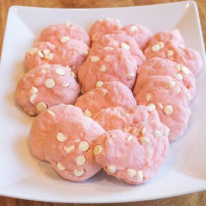 a plate of pink cookies, circular and heart shaped and with white chocolate chips.