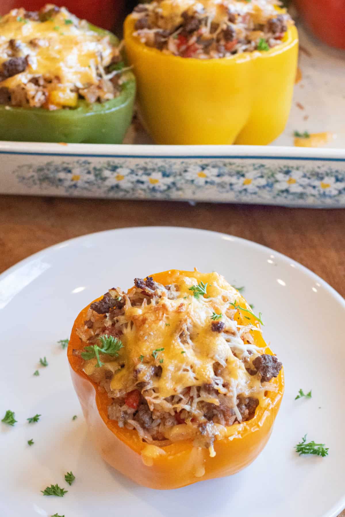 a stuffed pepper on a plate baked with cheese on top in front of a baking dish.