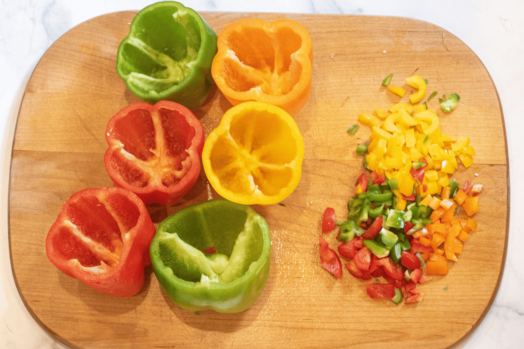6 colored bell peppers on a cutting board, empty, and diced pepper next to them.