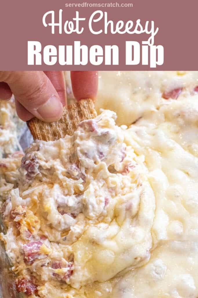 a hand holding a cracker dipping it into a Reuben dip with melted cheese and Pinterest pin text.