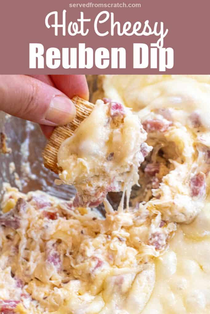 a hand holding a cracker dipping it into a Reuben dip with melted cheese and Pinterest pin text.