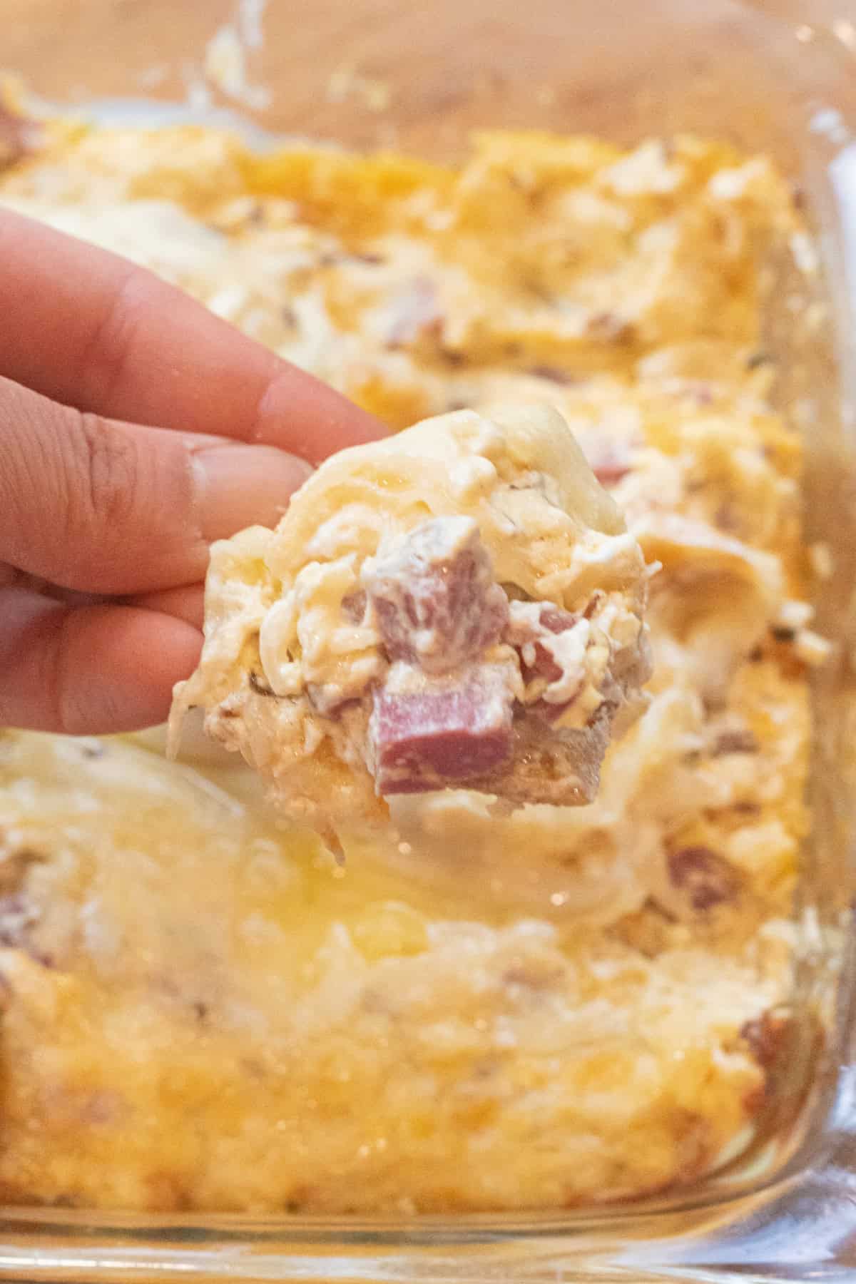 a hand holding a cracker dipping it into a Reuben dip with melted cheese.