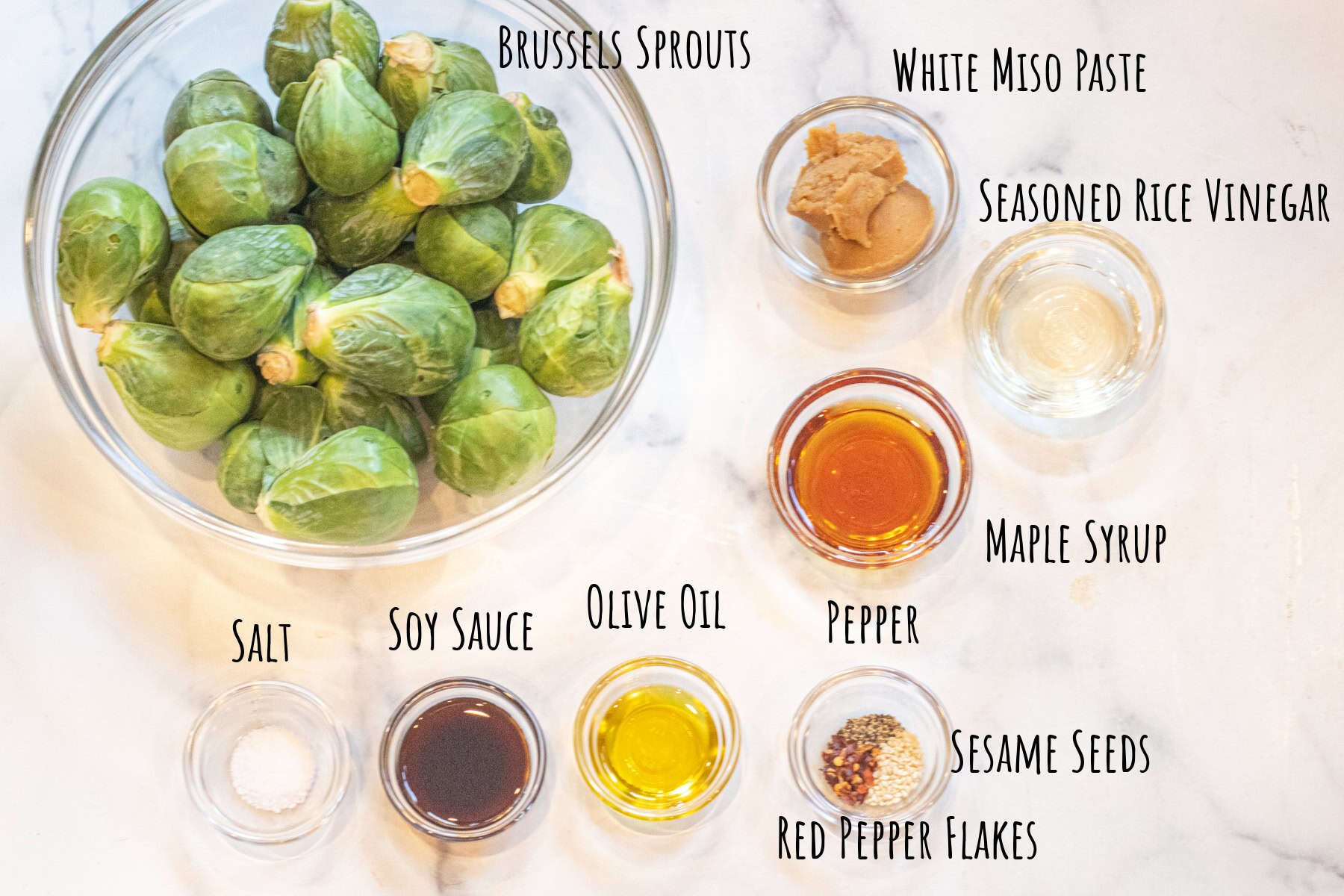 a bowl of Brussels sprouts and bowls of miso, rice vinegar, soy sauce, salt, olive oil, maple syrup, black pepper, sesame seeds, aand red pepper flakes.