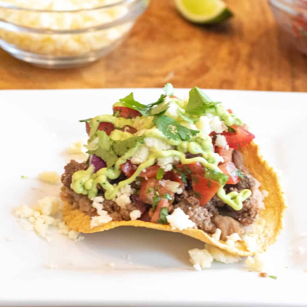 a plate with a loaded tostada with beef, pico, cotija, avocado cream sauce, and cilantro.