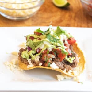 a plate with a loaded tostada with beef, pico, cotija, avocado cream sauce, and cilantro.