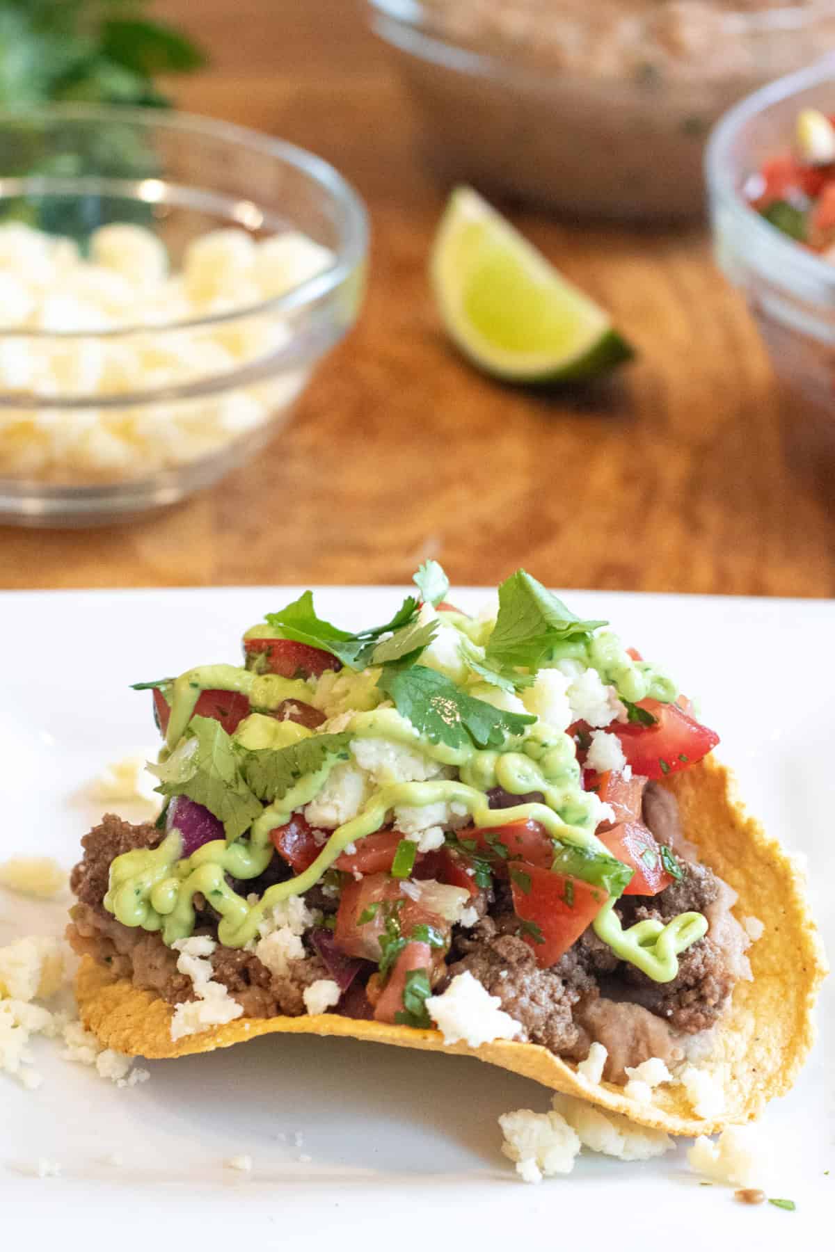 a plate with a loaded tostada with beef, pico, cotija, avocado cream sauce, and cilantro.