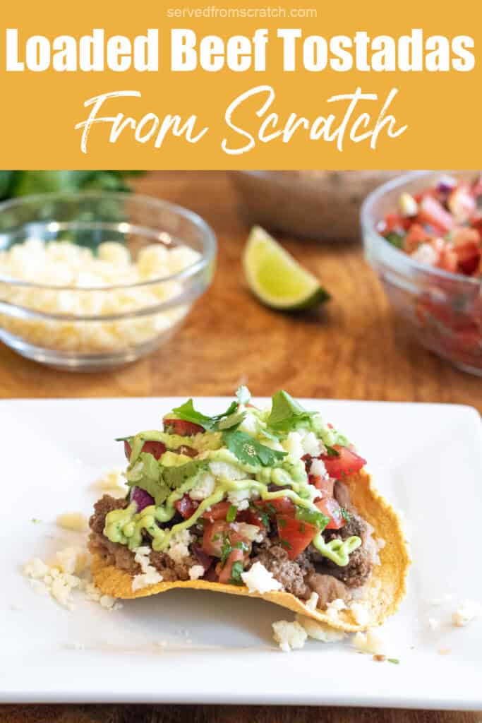 a loaded beef tostada on a plate with ground beef, cheese, pico, and a sauce, and Pinterest pin text.
