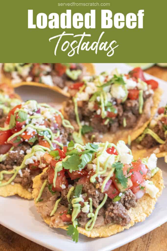 a plate with loaded beef tostadas with beans, beef, pico, cotija, cilantro, and avocado cream sauce and Pinterest pin text.