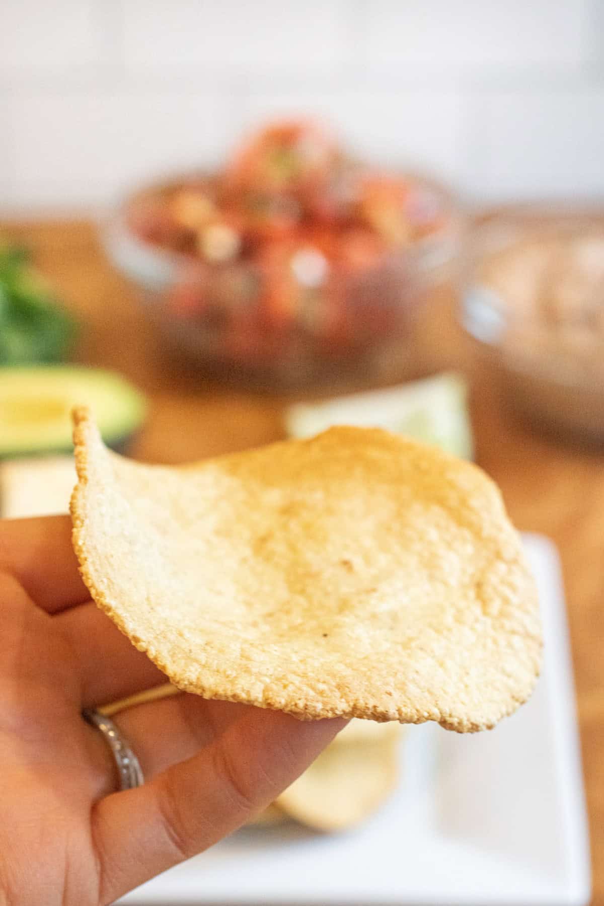 a hand holding a baked tostada shell.