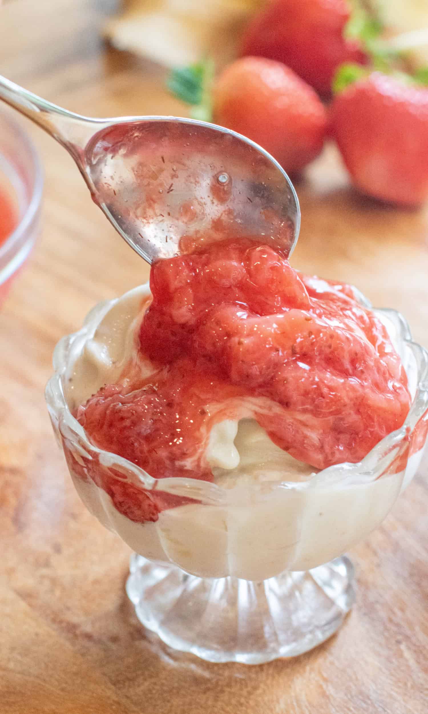 a small bowl of soft serve ice cream with a spoon of strawberry compote being added.