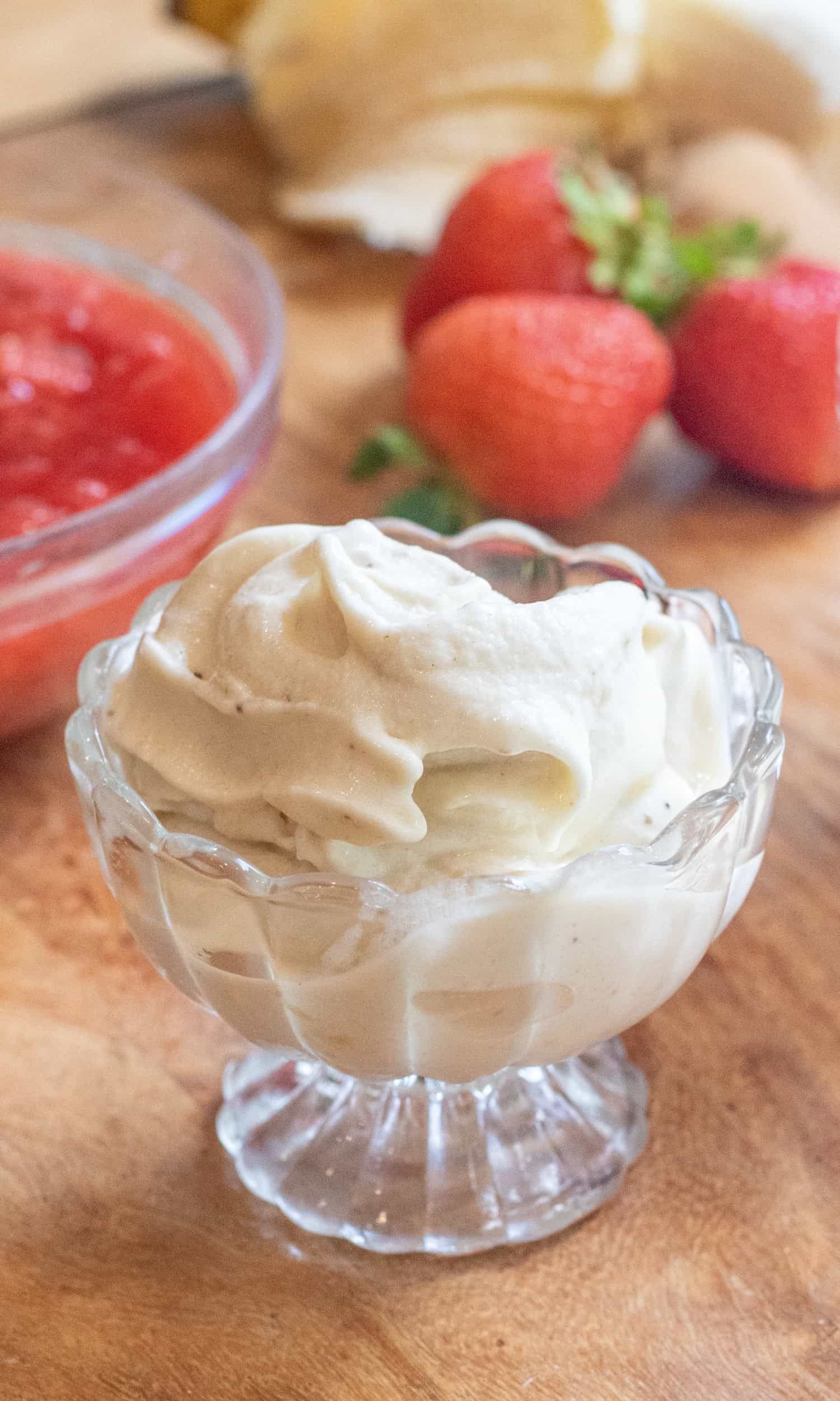 a small bowl of soft serve ice cream in front of strawberries and a bowl of compote.