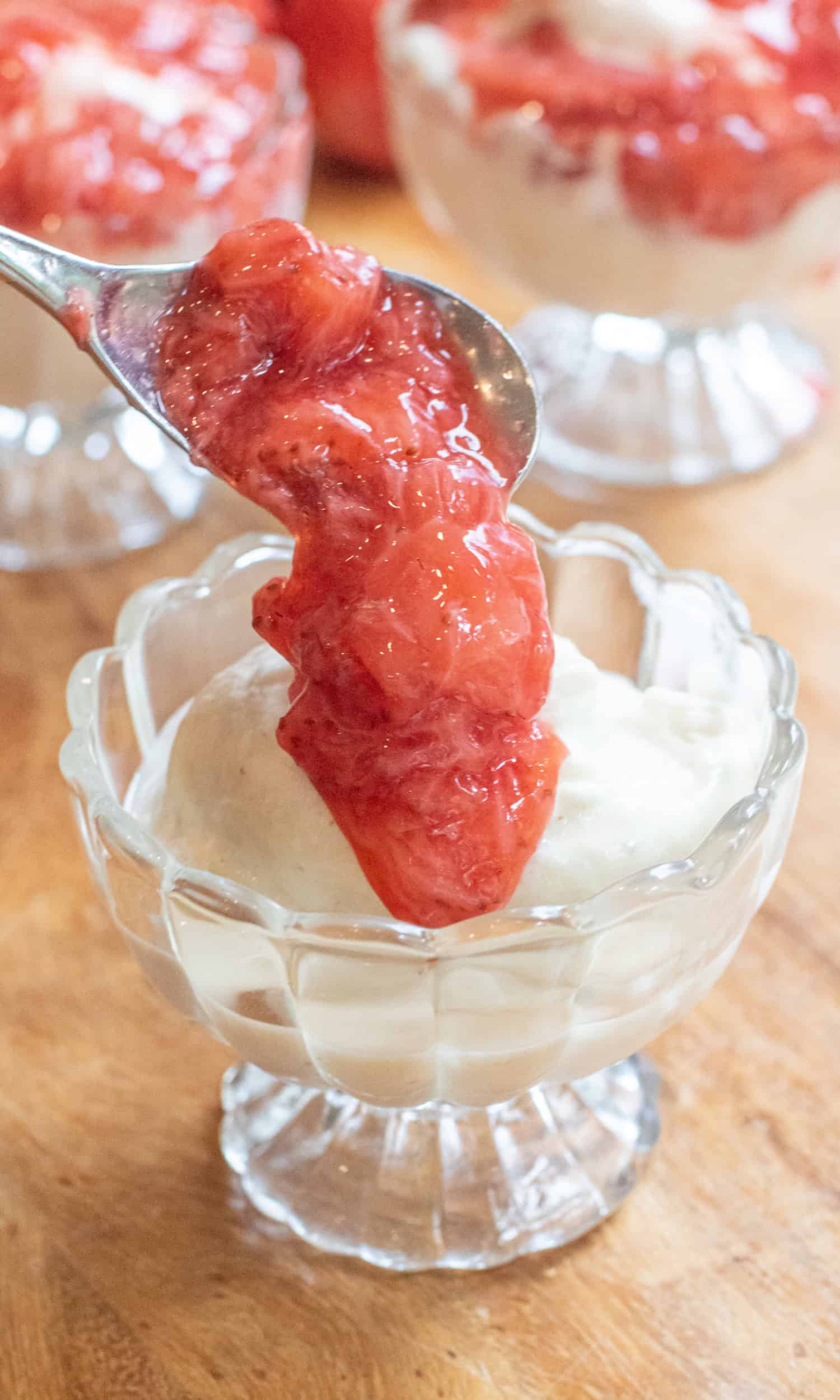 a small bowl of soft serve ice cream with a spoon of strawberry compote being added.
