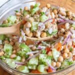 a bowl of chickpeas, beans, cucumber, tomatoes, onions, and feta with a spoonful in a wooden spoon.