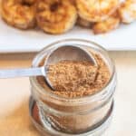 a small mason jar with a spoon and a seasoning mix in front of a plate of cooked seasoned shrimp.