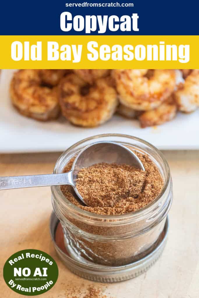 an overhead of a small mason jar of a spice blend mix with a measuring spoon next to it an some split in front of a plate of cooked shrimp.
