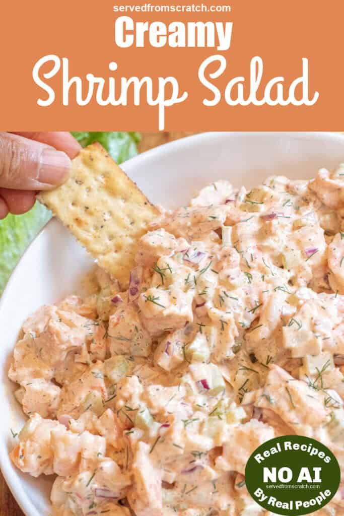 an overhead of a big bowl of creamy shrimp salad with a hand dipping in a cracker with Pinterest pin text and NO AI sticker.