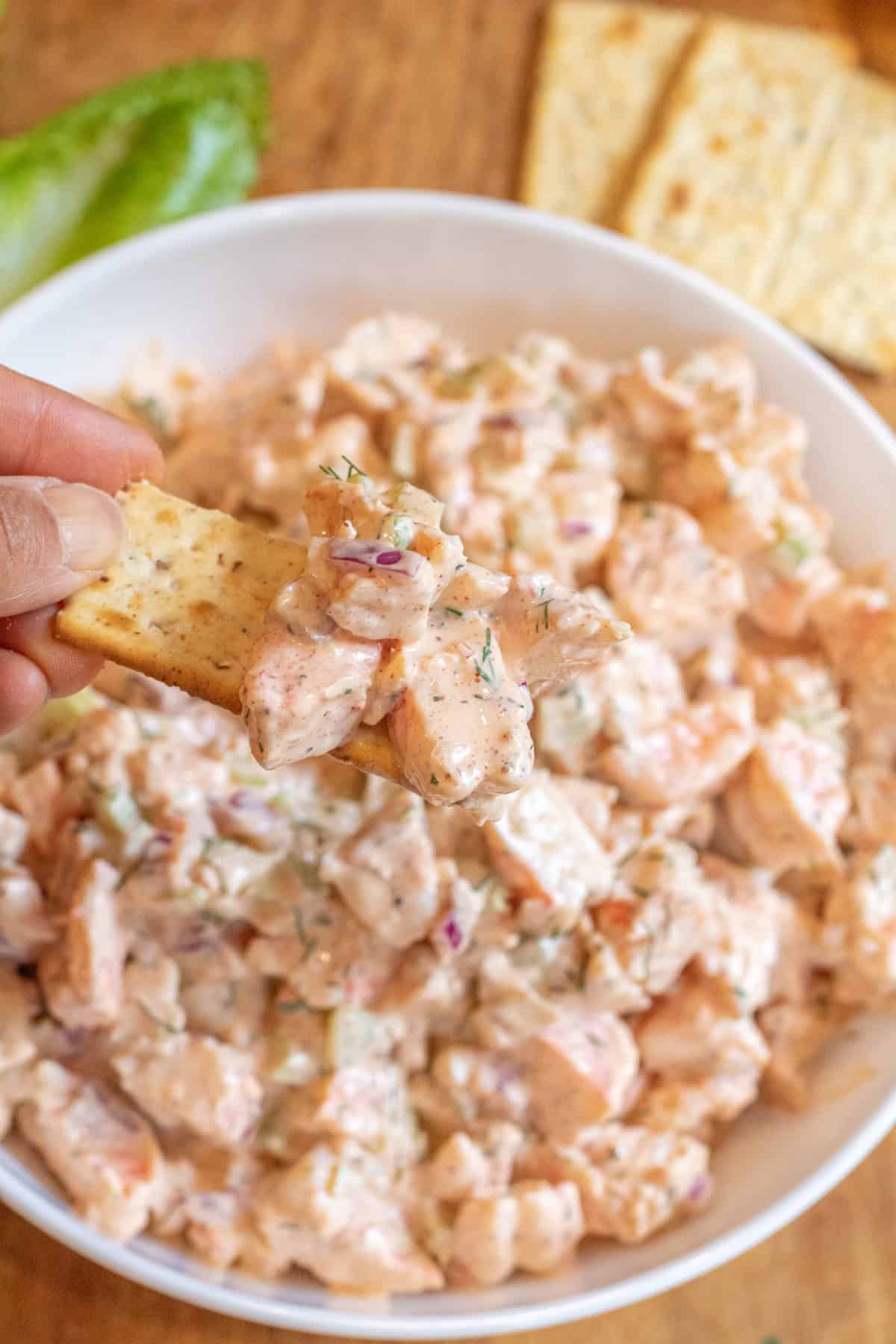 an overhead of a big bowl of creamy shrimp salad with a hand dipping in a cracker.