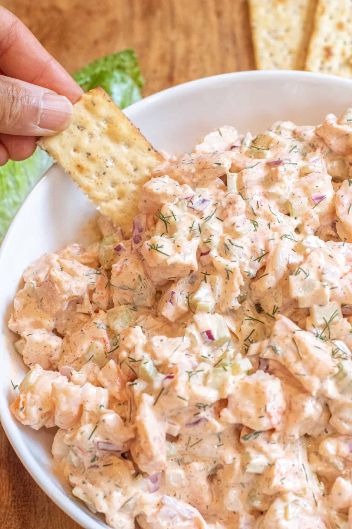 an overhead of a big bowl of creamy shrimp salad with a hand dipping in a cracker.