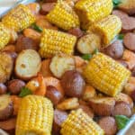an overhead of a sheet pan with cooked corn on the cob pieces, shrimp, and potatoes.