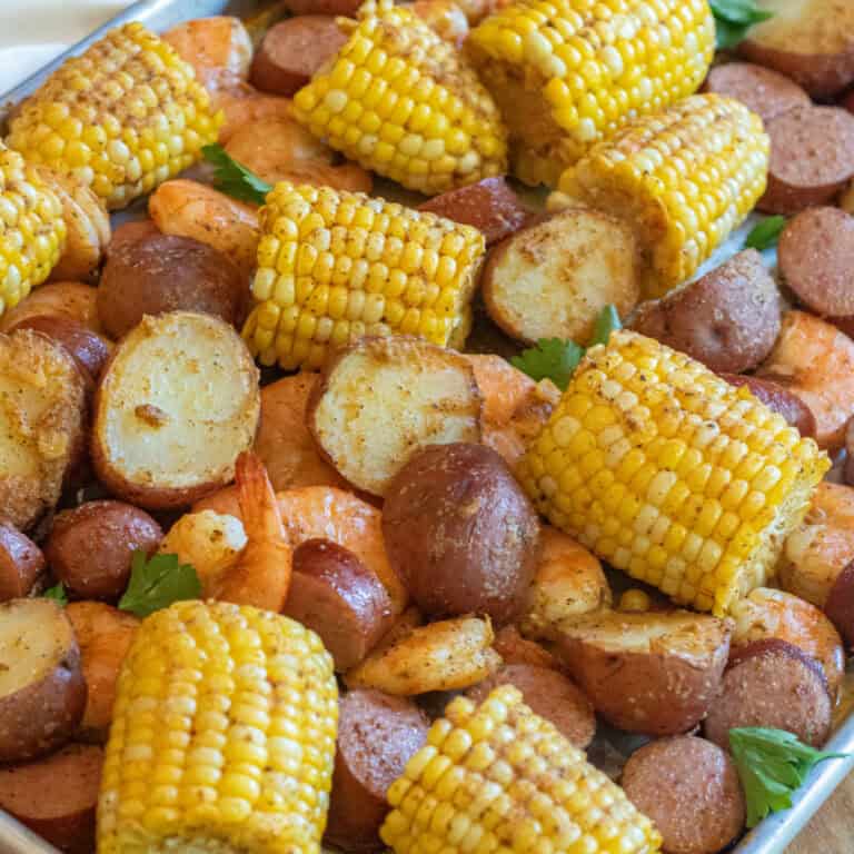 an overhead of a sheet pan with cooked corn on the cob pieces, shrimp, and potatoes.