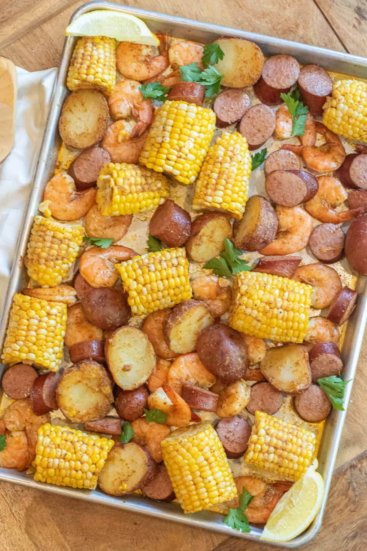 an overhead of a sheet pan with cooked corn on the cob pieces, shrimp, and potatoes.