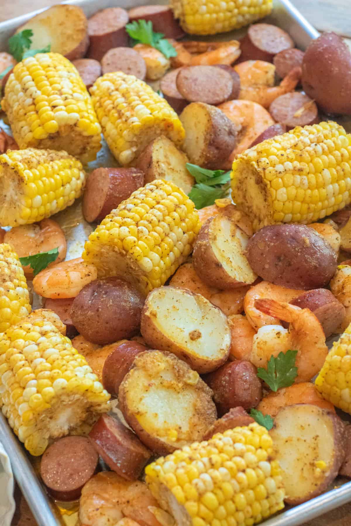 an overhead of a sheet pan with cooked corn on the cob pieces, shrimp, and potatoes.
