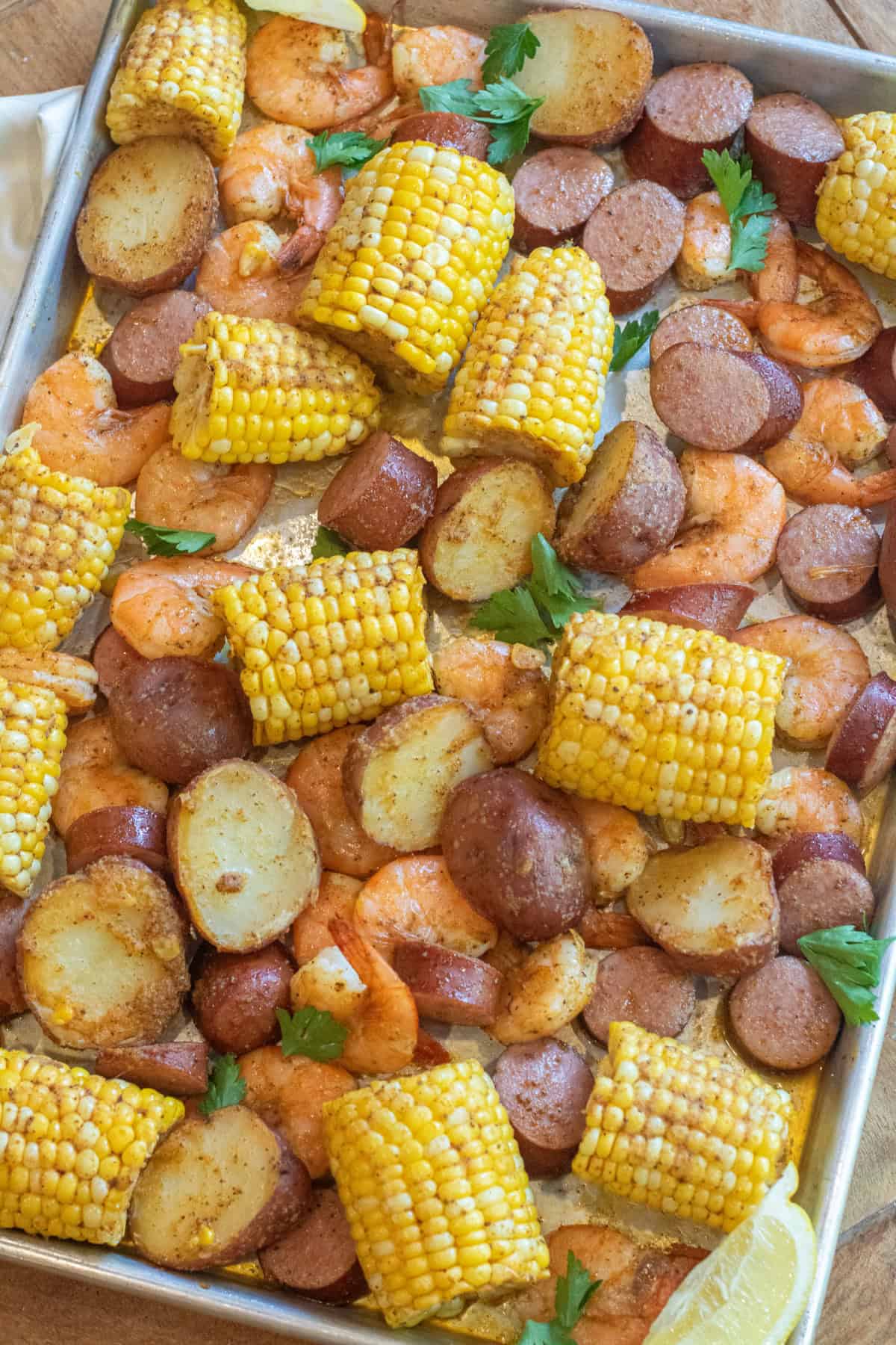 an overhead of a sheet pan with cooked corn on the cob pieces, shrimp, and potatoes.