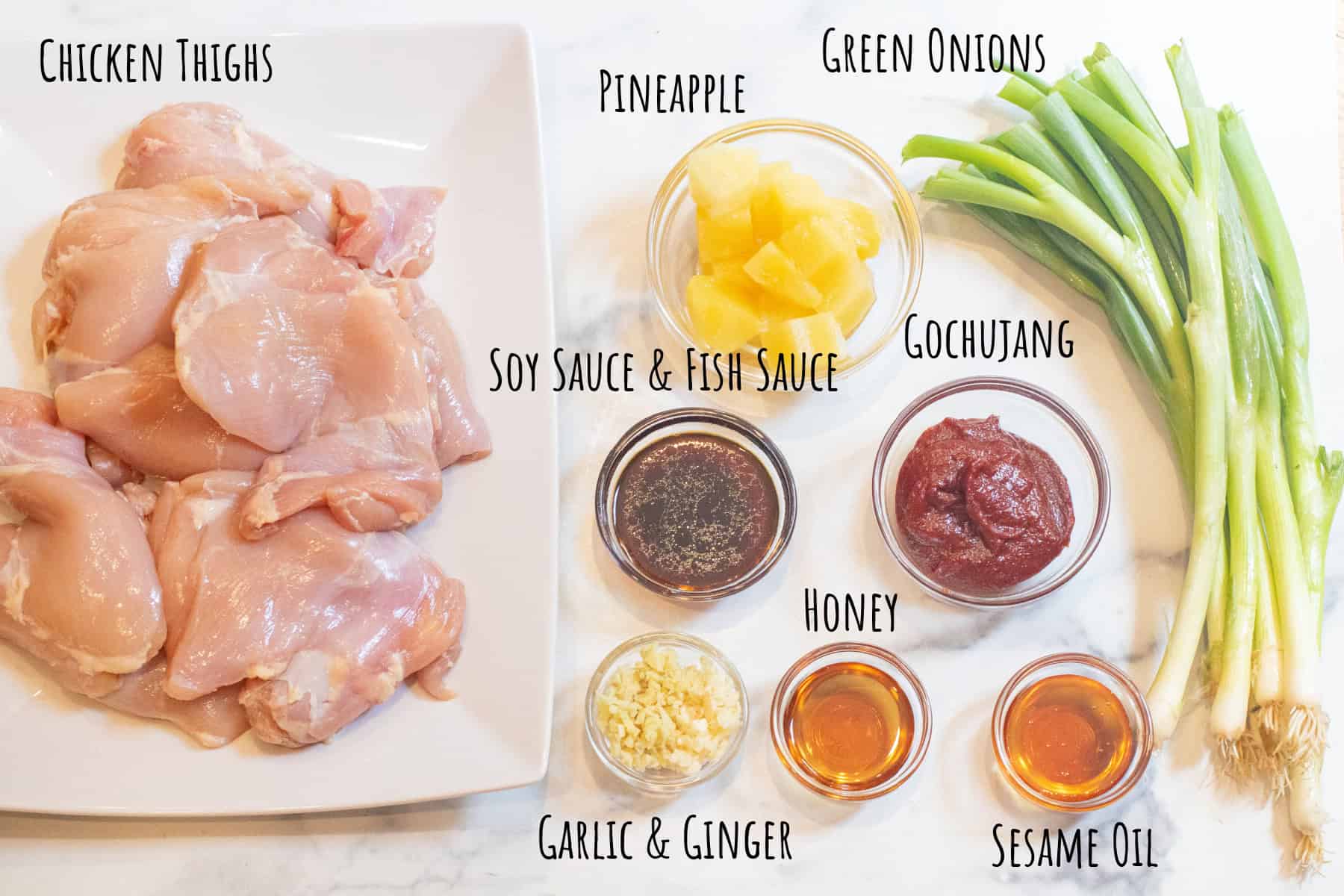 a plate of raw chicken thighs, bowls of pineapple, soy sauce, fish sauce, gochujang, minced garlic and ginger, honey, sesame oil, and green onions all labeled.