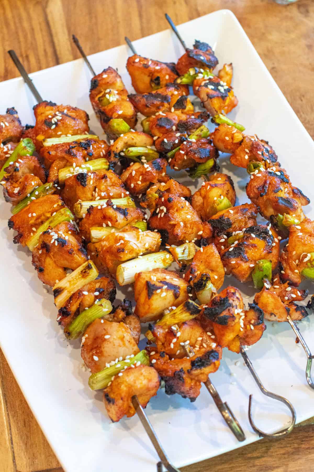 a large plate of grilled chicken skewers with green onion and sesame seeds.