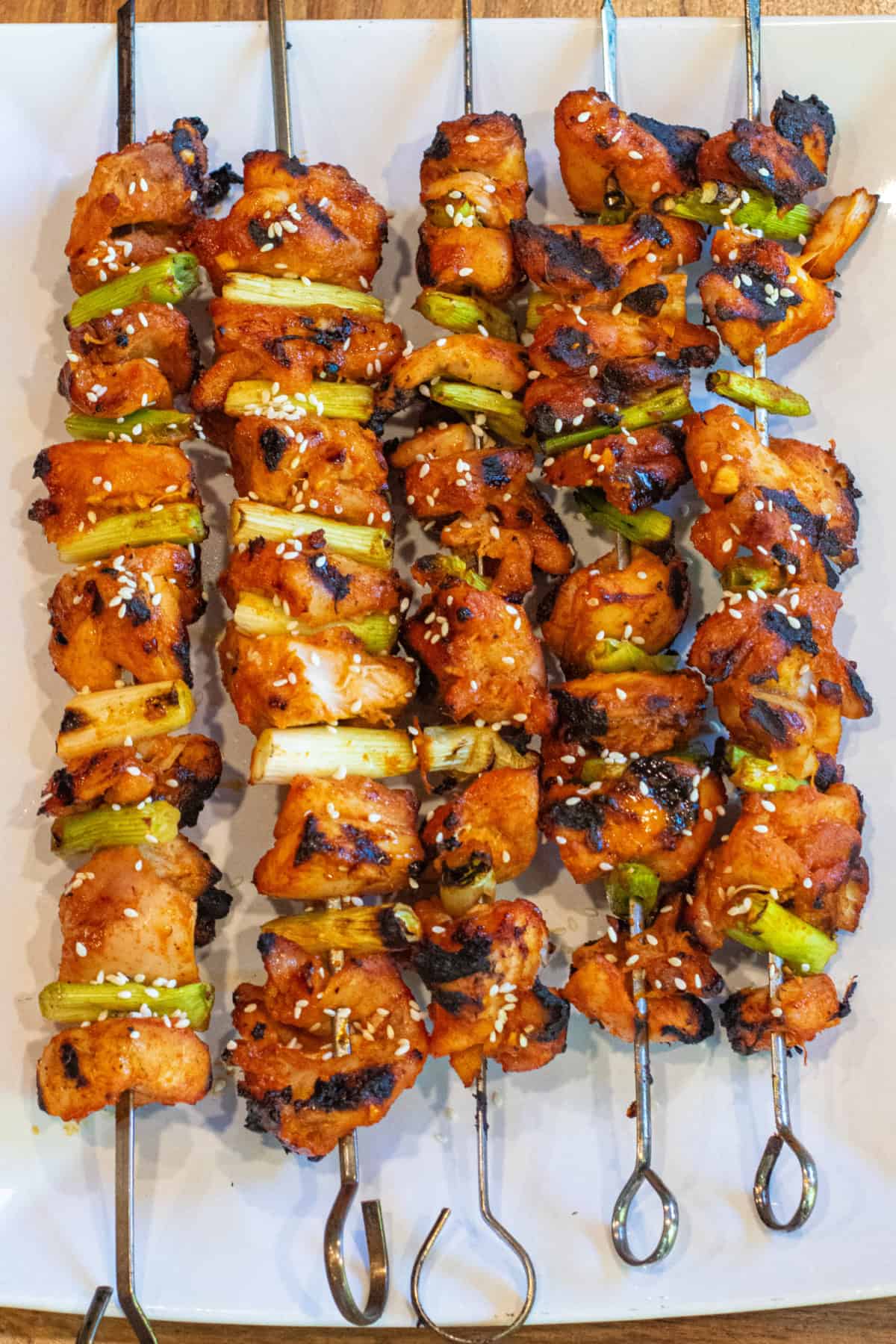 a large plate of grilled chicken skewers with green onion and sesame seeds.