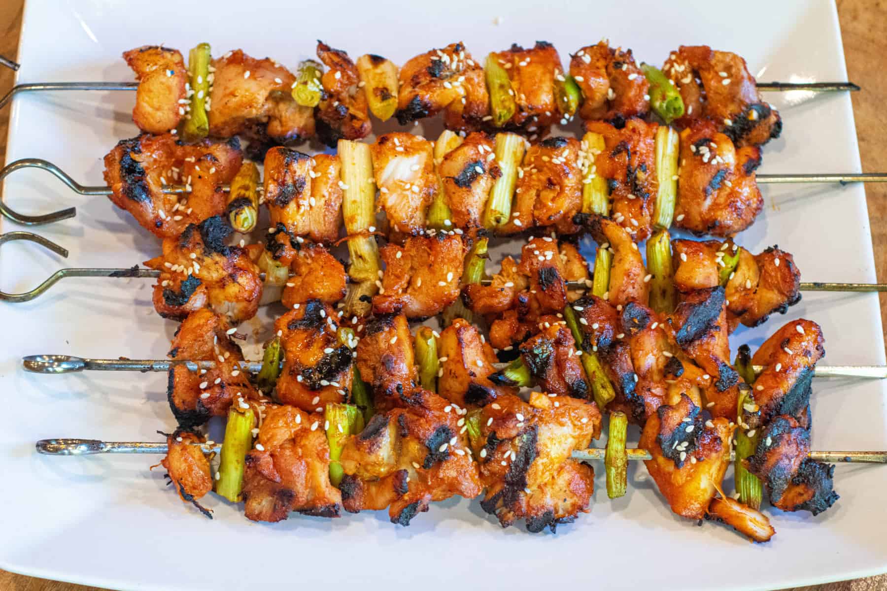 a large plate of grilled chicken skewers with green onion and sesame seeds.