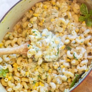 an overhead of a dutch oven with a wooden spoon in a creamy pasta with basil and shredded zucchini.