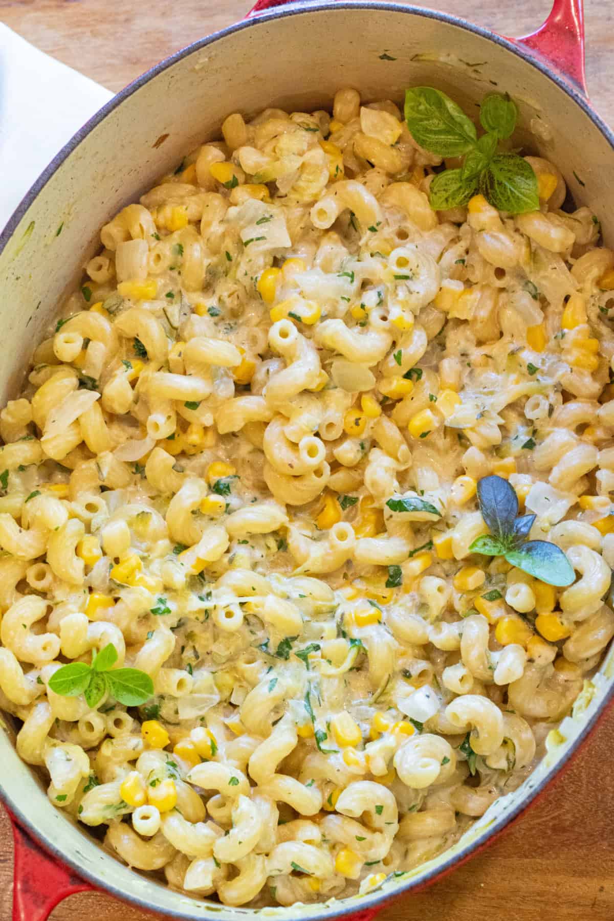 an overhead of a dutch oven with cooked pasta and creamy cheese and fresh basil.