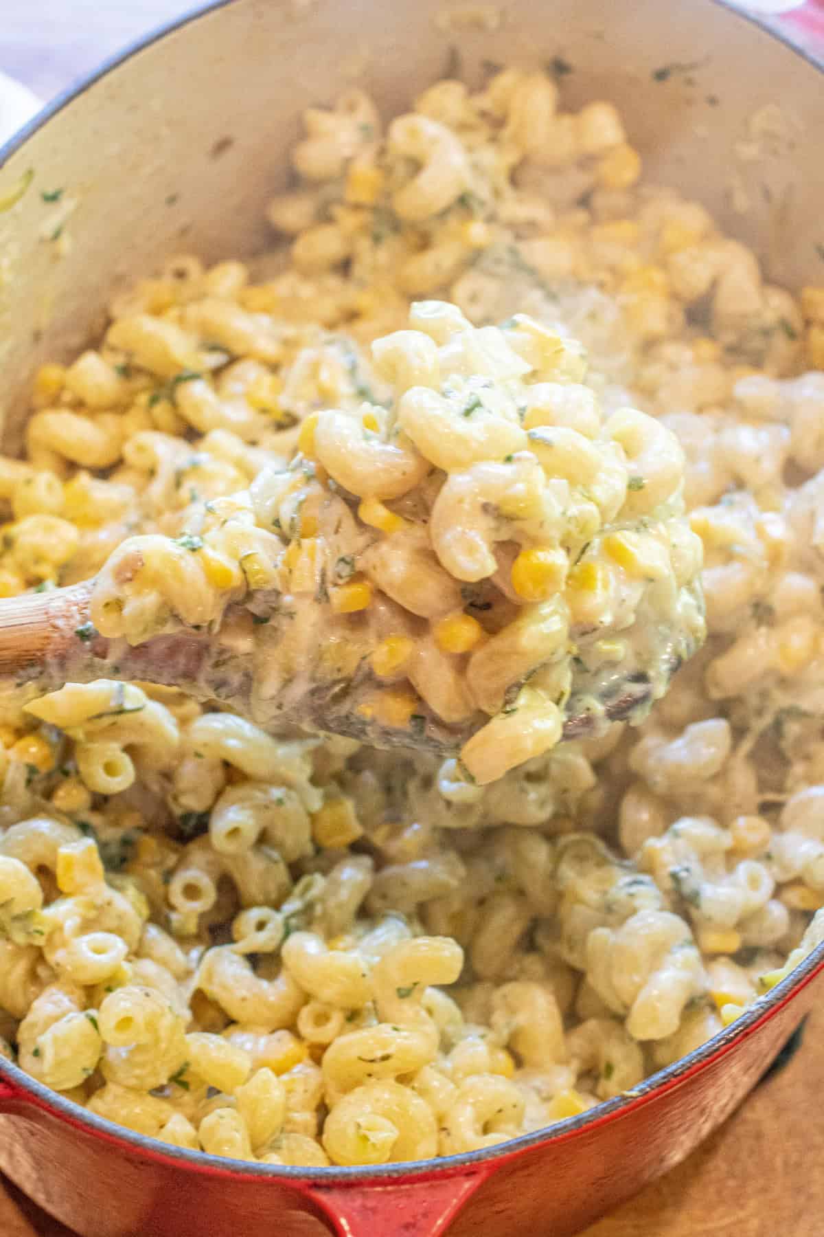 an overhead of a dutch oven with cooked pasta and creamy cheese and a wooden spoon with a creamy scoop.
