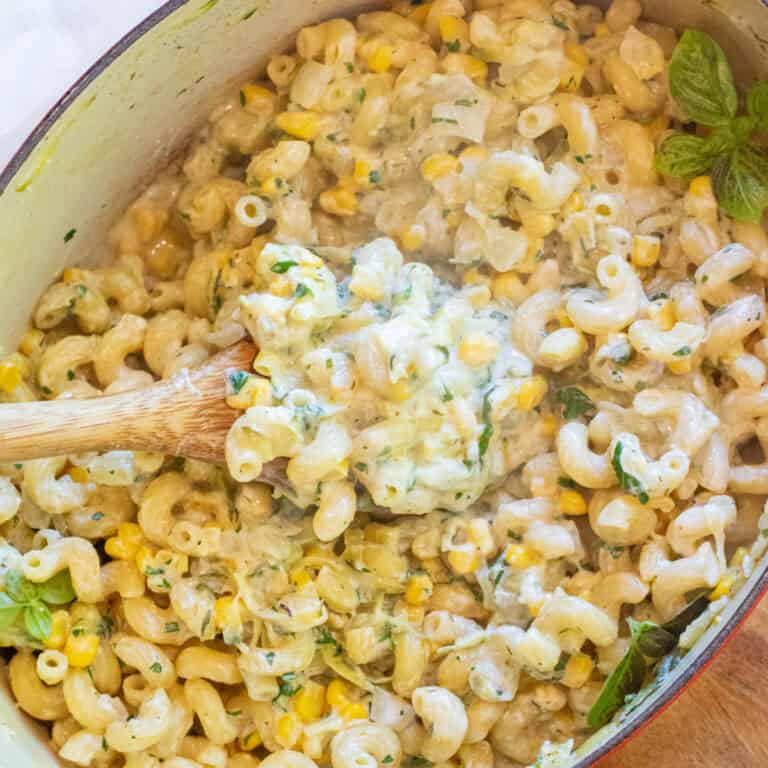 an overhead of a dutch oven with a wooden spoon in a creamy pasta with basil and shredded zucchini.