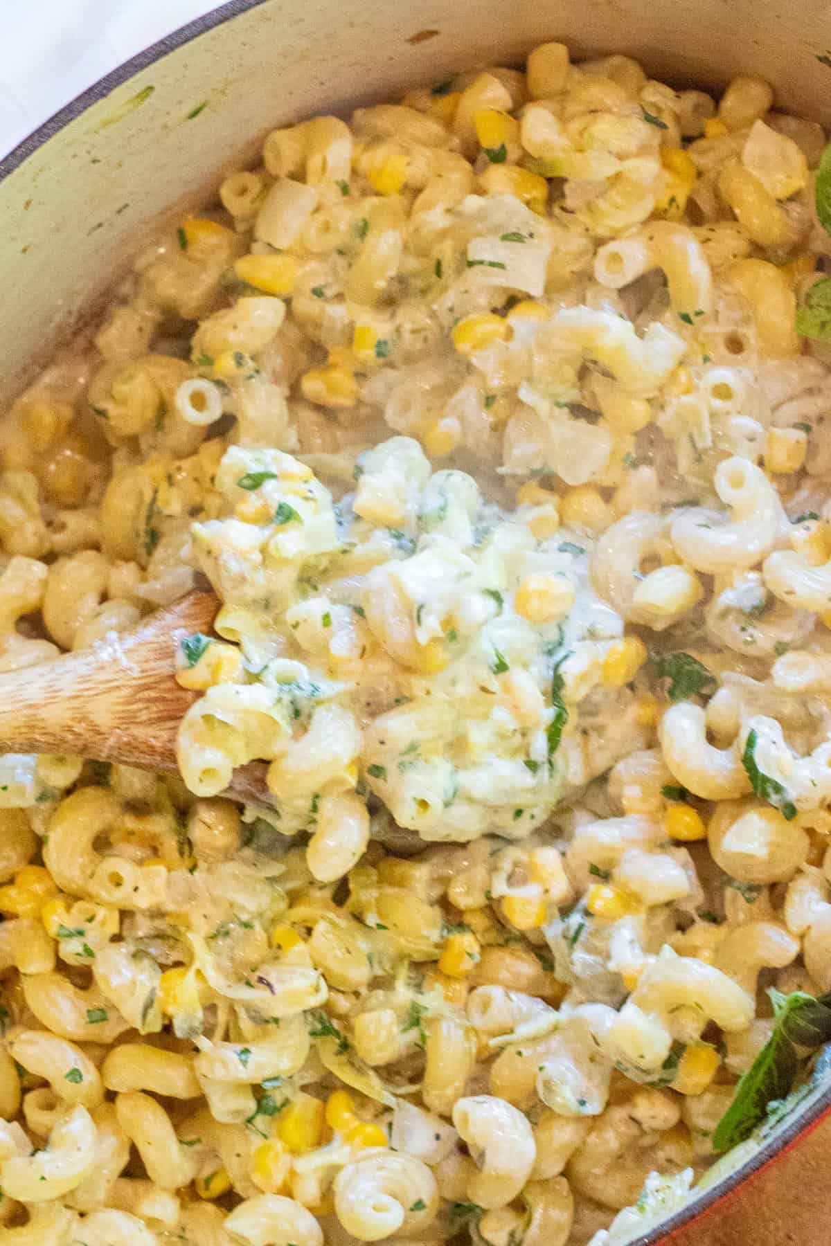 an overhead of a dutch oven with cooked pasta and creamy cheese and a wooden spoon with a creamy scoop.
