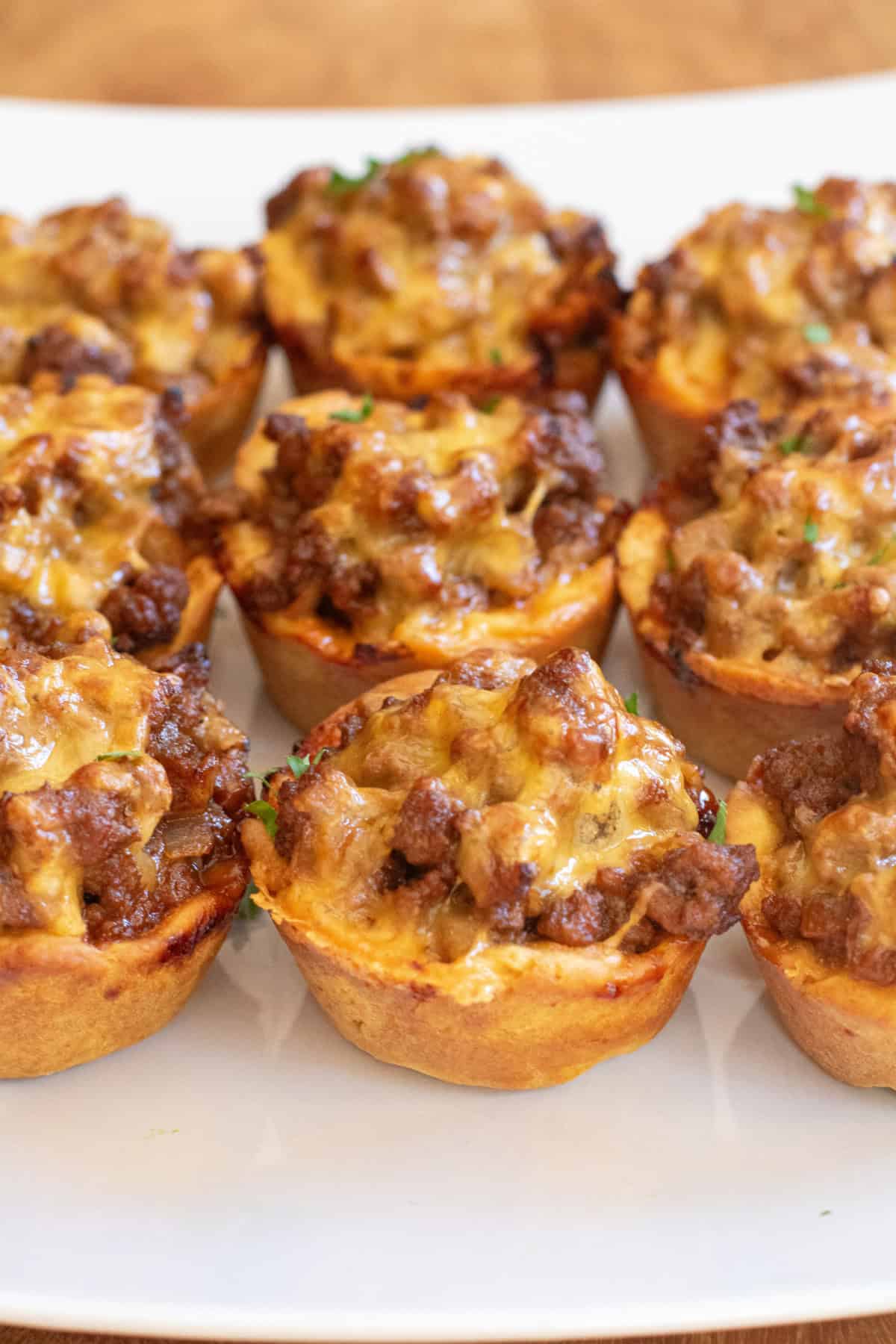 a plate full of baked pastry cups with ground beef and melted cheese on top.