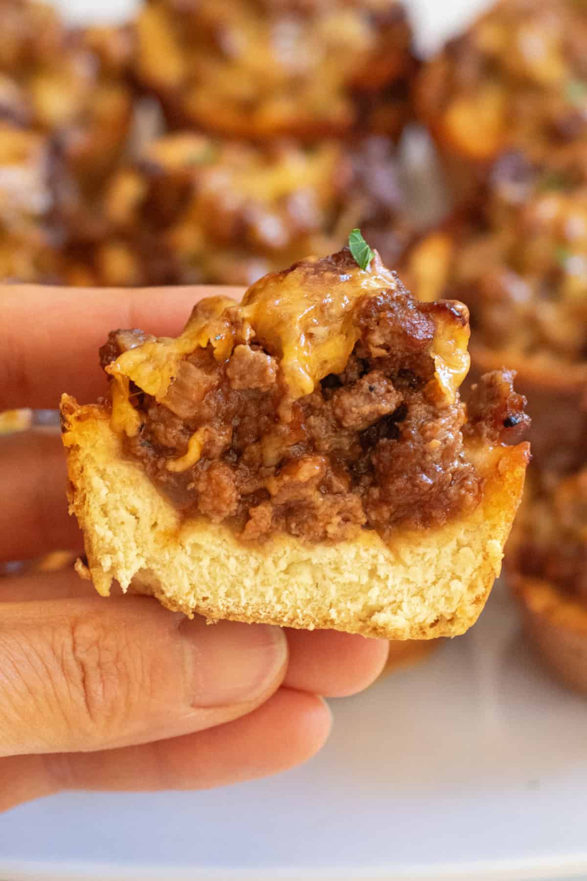 a hand holding a halved baked pastry cup of ground beef and melted cheese.