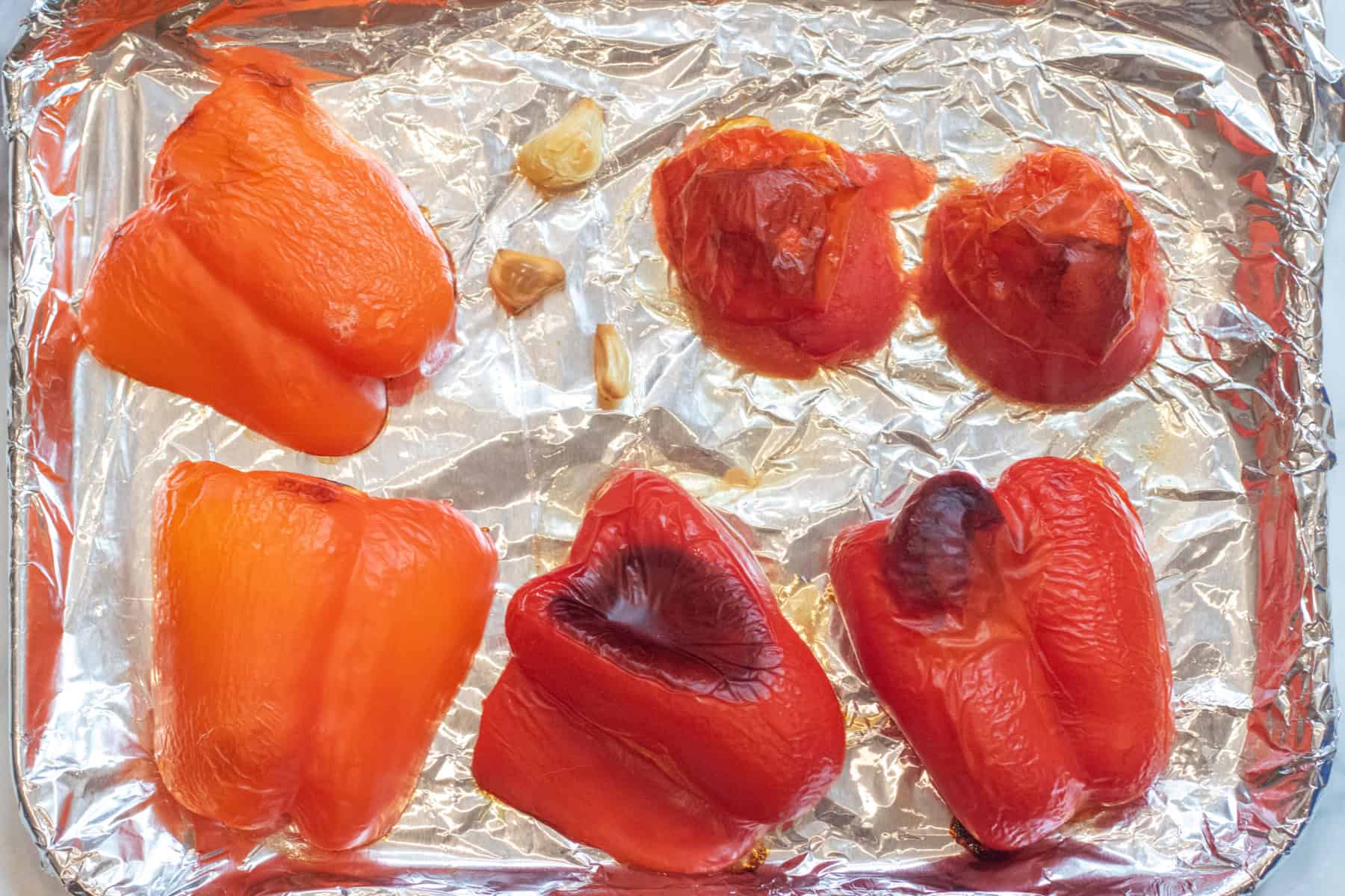 a tray of roasted red bell peppers, tomato, and garlic on a foil lined tray.