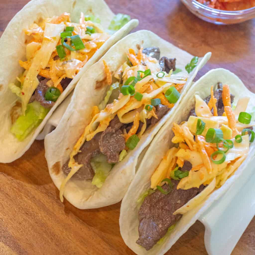 an overhead of 3 tacos in a taco holder with beef, slaw, and green onions on top.