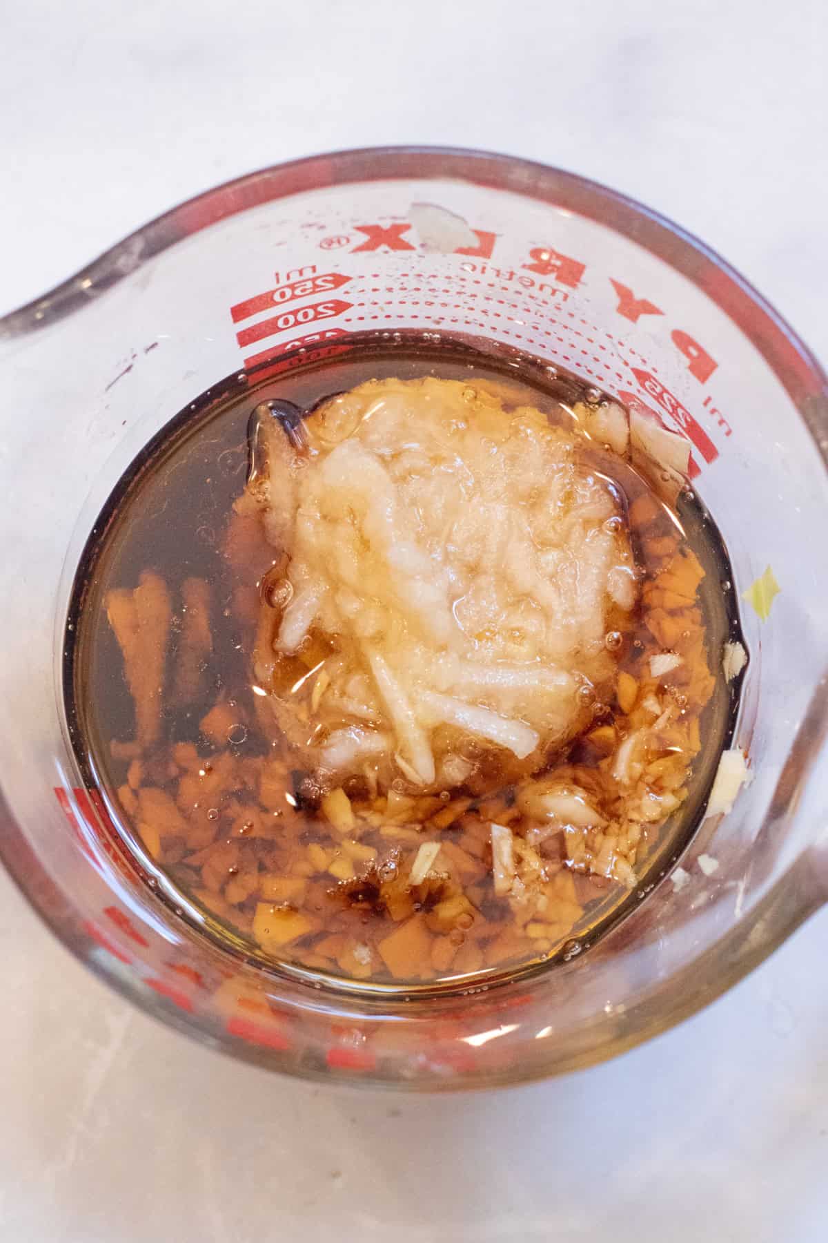 an overhead of a pyrex with oil, soy, shredded pear, and garlic.