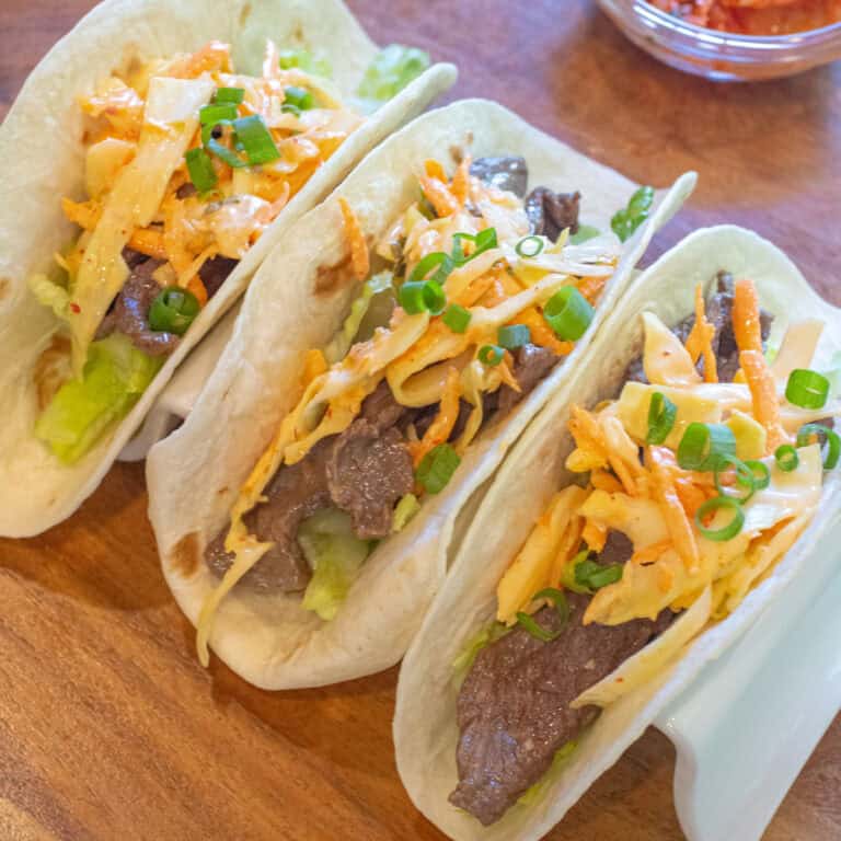 an overhead of 3 tacos in a taco holder with beef, slaw, and green onions on top.